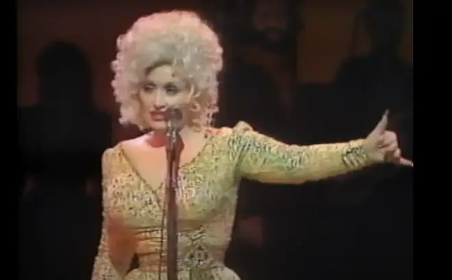 Dolly Parton doing an impression of Elvis Presley is the best thing we've seen in ages. Pictured in London in 1983.